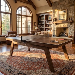 May include: A contemporary dark wood ping pong table with a net, bats, and balls is positioned on a patterned rug in a large living room. The room includes a piano, fireplace, and large windows.