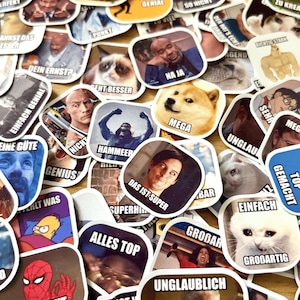 Op de afbeelding: Een verzameling diverse meme-stickers met verschillende afbeeldingen en tekst. De stickers tonen populaire internetmemes met zinnen als "MEGA", "SEHR GUT" en "ALLES TOP". De stickers zijn in verschillende vormen en maten.