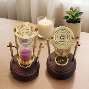 May include: Two decorative hourglasses with brass frames and wooden bases. One has the text "The future depends on what you do today." The other reads "Made for Royal Navy London." Both contain pink sand.