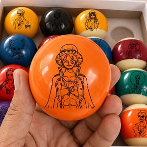 May include: A set of billiard balls with character illustrations in a white box. The balls are various colours, including orange, yellow, blue, red, and purple. A map scroll and a red gift box are in the background.