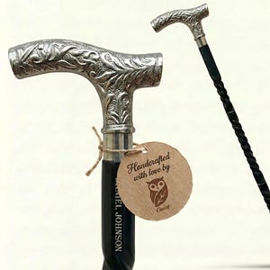 Puede incluir: Bastón plateado con un diseño floral ornamentado en el mango. El eje negro tiene un patrón retorcido. Una etiqueta marrón dice "Handcrafted with love by Owlcat."