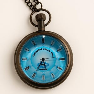 May include: Antique-style pocket watch with a blue face and Roman numerals. The watch has a bronze-colored casing and a matching chain. The face of the watch reads "Colonial Clock Co. 1872 London."
