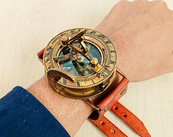 May include: A vintage brass sundial watch with a leather strap. The watch face features Roman numerals and the text "West London." The watch has a compass and is attached to a red leather strap.