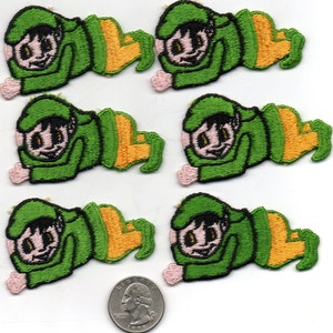 Puede incluir: Seis parches bordados de hierro verde y amarillo de un duende de dibujos animados con un sombrero verde, piel rosa y ojos negros. El duende está acostado boca abajo con los brazos extendidos.