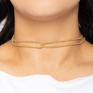 May include: A gold chain choker necklace with a double layer design. The necklace has a simple, minimalist style.