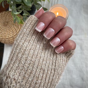 May include: A hand with a light pink and white french manicure. The nails are long and oval shaped.