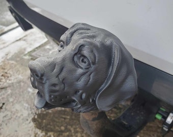 May include: A black 3D printed dog head hitch cover. The dog has a realistic expression with a slightly open mouth and a textured surface.