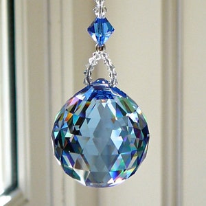 Peut inclure: Un capteur de soleil en cristal suspendu avec une boule de cristal bleue à facettes en bas. Le capteur de soleil a une chaîne de perles transparentes et deux accents de cristal bleu. L'arrière-plan montre une fenêtre.