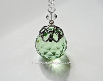 Op de afbeelding: Een facetgeslepen, lichtgroene kristallen bolhanger met een zilverkleurige filigraankap en een ketting van heldere kristallen kralen. De hanger werpt een schaduw op een wit oppervlak. Tekst op de afbeelding luidt "HeartstringsByMorgan.etsy.com".