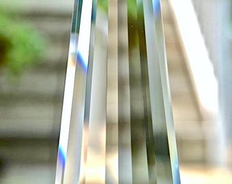 May include: A clear crystal prism with a faceted design. The prism is hanging from a silver chain.