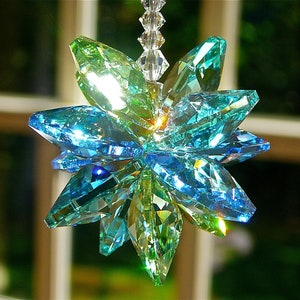 May include: A crystal suncatcher with a starburst design in shades of blue and green. The suncatcher is made of faceted crystal and hangs from a silver chain.