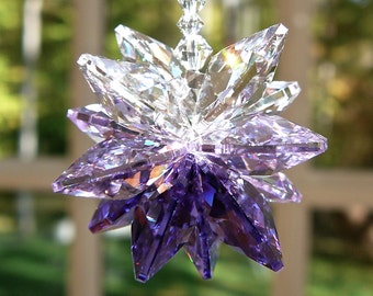 Peut inclure: Un ornement en cristal à facettes en forme d'étoile, présentant un dégradé de couleurs passant du transparent en haut au violet profond et saturé en bas. L'ornement est suspendu par une chaîne de petites perles en cristal transparent à facettes.