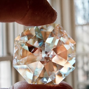 Peut inclure: Un prisme en cristal transparent et facetté de forme hexagonale. Le prisme réfléchit la lumière, créant un effet arc-en-ciel.