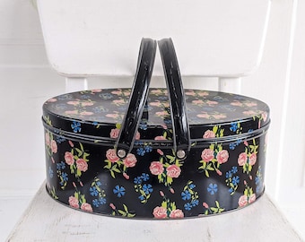 Pode incluir: Uma lata ovalada preta com um padrão floral em rosa, azul e verde. A lata tem duas alças pretas e está sentada em uma cadeira branca.