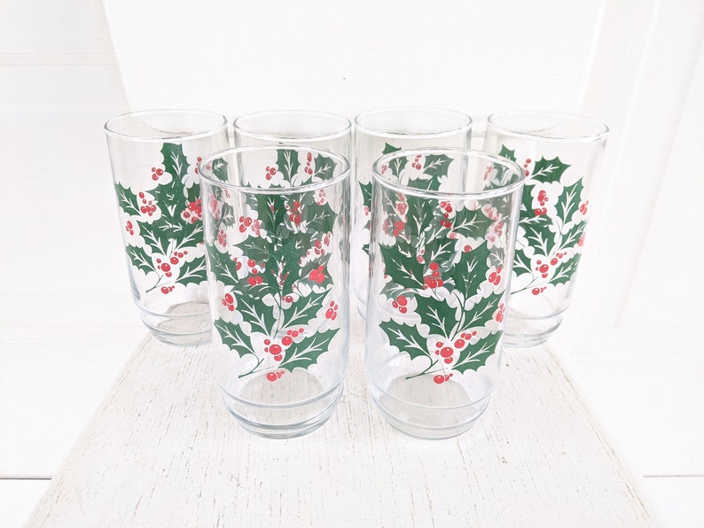 May include: Set of six clear glass drinking glasses with a holly and berry design. The glasses have a green holly leaf pattern with red berries.