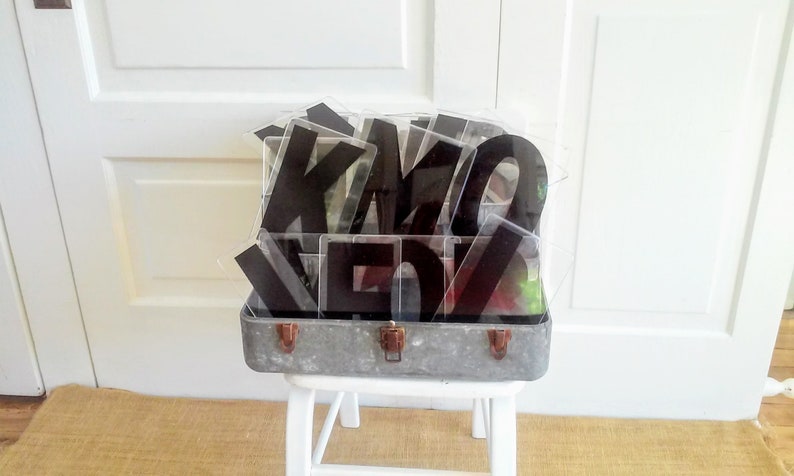 May include: A vintage metal suitcase filled with black acrylic letters. The letters are in a clear plastic container and spell out the word "KIMO"