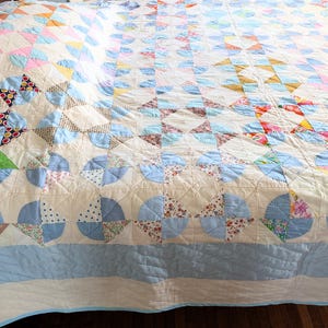 Puede incluir: Un edred&oacute;n vintage con un dise&ntilde;o de patchwork. El edred&oacute;n presenta un fondo color crema con varios patrones geom&eacute;tricos en tonos de azul, rosa, marr&oacute;n y estampados florales. El edred&oacute;n probablemente est&aacute; hecho de algod&oacute;n y tiene una textura acolchada.