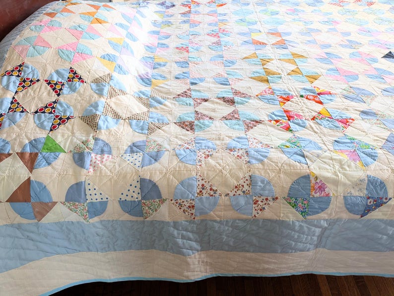 Puede incluir: Un edred&oacute;n vintage con un dise&ntilde;o de patchwork. El edred&oacute;n presenta un fondo color crema con varios patrones geom&eacute;tricos en tonos de azul, rosa, marr&oacute;n y estampados florales. El edred&oacute;n probablemente est&aacute; hecho de algod&oacute;n y tiene una textura acolchada.
