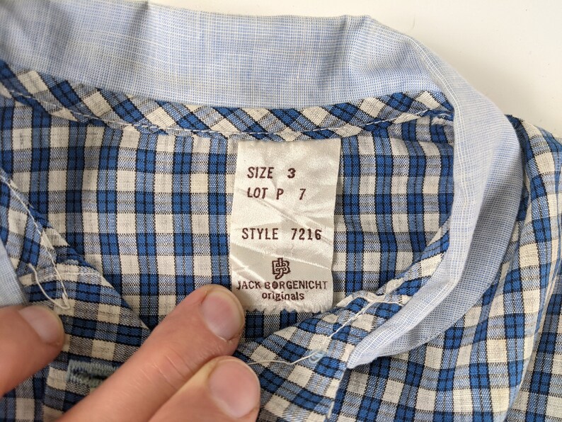 Op de afbeelding: Een blauw-wit geruit overhemd met een label met de tekst "SIZE 3 LOT P 7 STYLE 7216 JACK BORGENSICHT originals".