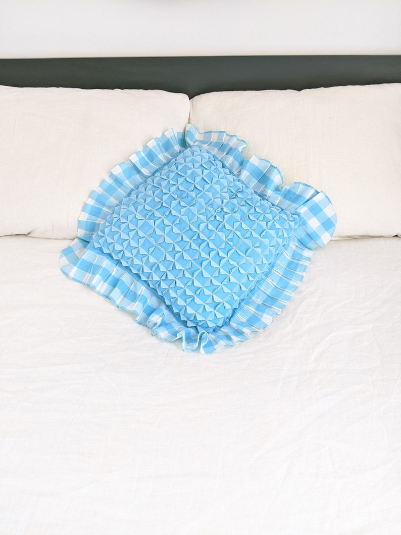 Op de afbeelding: Een blauw en wit geruit kussen met een gerimpelde rand en een blauw gestikt midden.