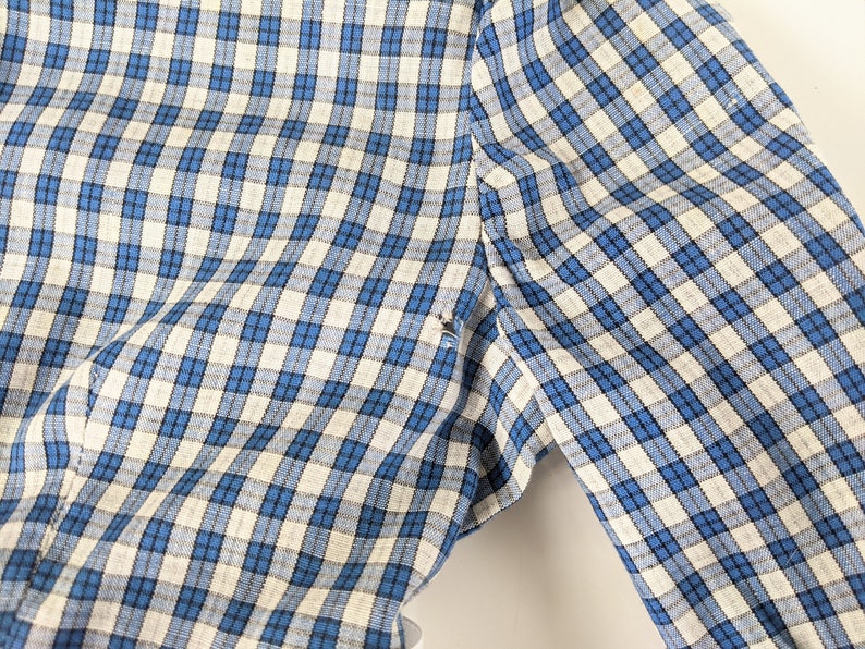 Op de afbeelding: Een blauwe en witte geruite stof met een subtiele textuur. De stof is gevouwen en laat het patroon zien.