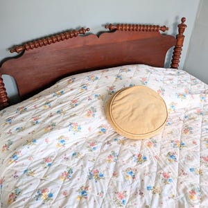 Puede incluir: Un marco de cama de madera con un edred&oacute;n con estampado floral y un coj&iacute;n redondo de color beige. La cabecera es de color marr&oacute;n oscuro con husillos decorativos. El edred&oacute;n presenta un fondo blanco con racimos de flores coloridas.