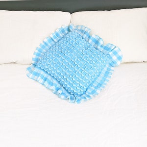 Op de afbeelding: Een blauw en wit geruit kussen met een gerimpelde rand. Het kussen is gevuld met een zacht, pluizig materiaal dat een textuur cre&euml;ert.