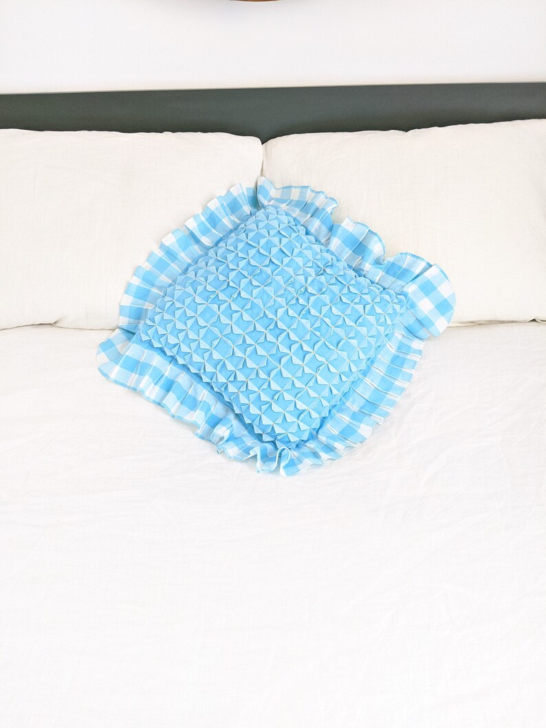 Op de afbeelding: Een blauw en wit geruit kussen met een gerimpelde rand. Het kussen is gevuld met een zacht, pluizig materiaal dat een textuur cre&euml;ert.