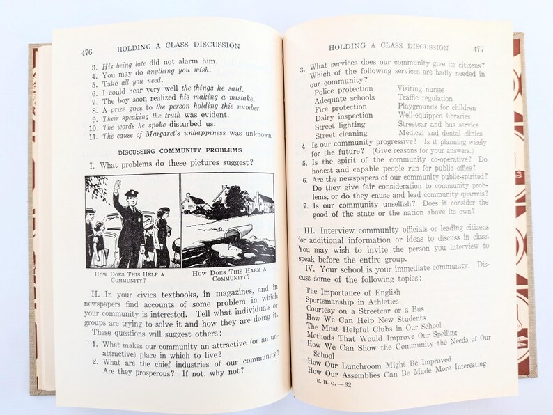 K&ouml;nnte beinhalten: Offenes Buch mit Text und Illustrationen. Seite 476 zeigt eine Diskussion &uuml;ber Gemeinschaftsprobleme mit Fragen und Bildern. Seite 477 setzt die Diskussion mit weiteren Fragen fort. Das Buch hat ein rot-cremefarbenes Farbschema.
