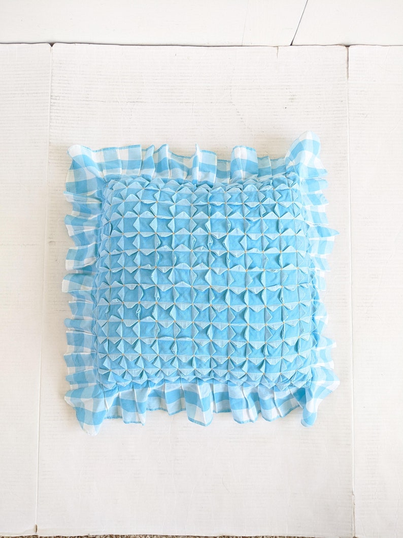 Op de afbeelding: Een blauw en wit geruit kussen met een gerimpelde rand. Het kussen is gevuld met een gestikt patroon dat een textuur cre&euml;ert.