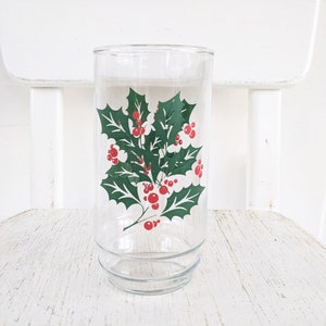 May include: A clear glass drinking glass with a green holly and red berry design.