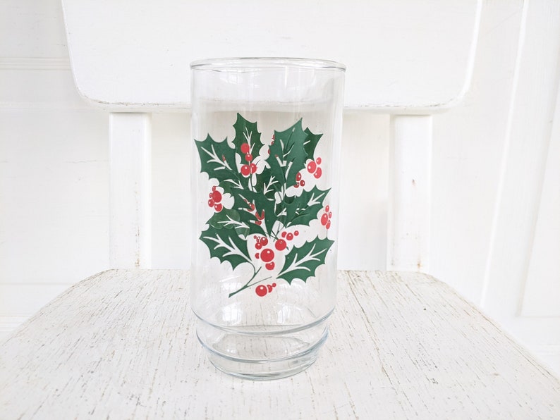 May include: A clear glass drinking glass with a green holly and red berry design.