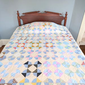 Puede incluir: Una colcha vintage con un dise&ntilde;o de patchwork colorido cubre una cama. La colcha presenta un fondo crema con patrones geom&eacute;tricos azules, rosas, amarillos y verdes. Se ve un cabecero de madera marr&oacute;n oscuro detr&aacute;s.