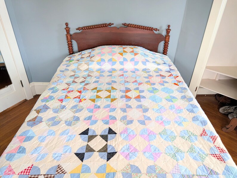 Puede incluir: Una colcha vintage con un dise&ntilde;o de patchwork colorido cubre una cama. La colcha presenta un fondo crema con patrones geom&eacute;tricos azules, rosas, amarillos y verdes. Se ve un cabecero de madera marr&oacute;n oscuro detr&aacute;s.