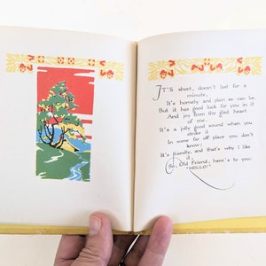 Pode incluir: Um livro aberto com uma capa amarela e uma ilustra&ccedil;&atilde;o colorida de uma &aacute;rvore e um riacho na p&aacute;gina da esquerda. A p&aacute;gina da direita tem texto que diz "It's short, doesn't last for a minute, It's homely and plain as can be, But it has good luck for you in it And joy from the glad heart of me. It's a jolly good sound when you strike it In some far off place you don't know: It's friendly, and that's why I like it, So, Old Friend, here's to you: "HELLO!"