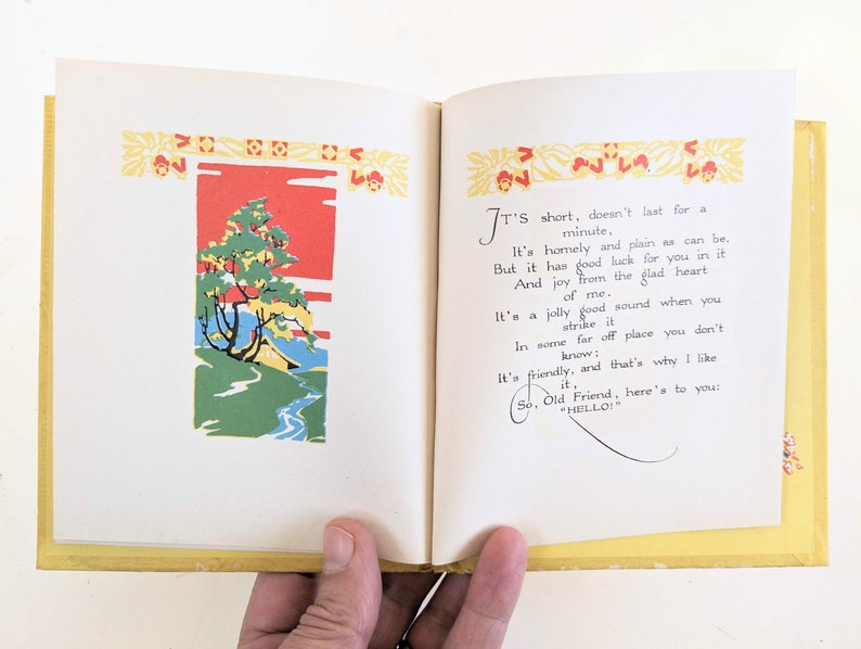 Pode incluir: Um livro aberto com uma capa amarela e uma ilustra&ccedil;&atilde;o colorida de uma &aacute;rvore e um riacho na p&aacute;gina da esquerda. A p&aacute;gina da direita tem texto que diz "It's short, doesn't last for a minute, It's homely and plain as can be, But it has good luck for you in it And joy from the glad heart of me. It's a jolly good sound when you strike it In some far off place you don't know: It's friendly, and that's why I like it, So, Old Friend, here's to you: "HELLO!"