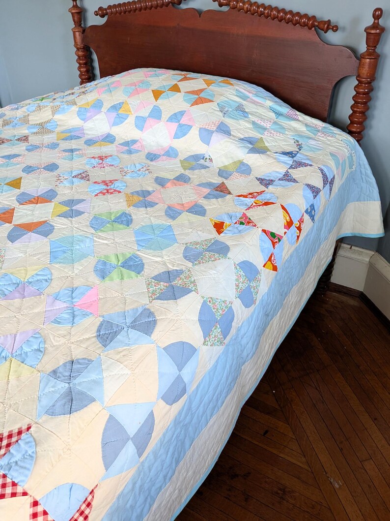 Puede incluir: Un edred&oacute;n hecho a mano con un patr&oacute;n de molinillo en colores pastel de azul, rosa, naranja y verde. El edred&oacute;n est&aacute; sobre una cama con cabecero de madera. El edred&oacute;n tiene un borde azul claro y un fondo color crema.