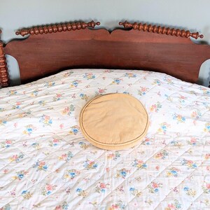 Puede incluir: Un marco de cama de madera vintage con acabado marr&oacute;n oscuro. El cabecero presenta husillos decorativos y una parte superior curvada. La cama est&aacute; hecha con un edred&oacute;n con estampado floral y una almohada redonda y beige.