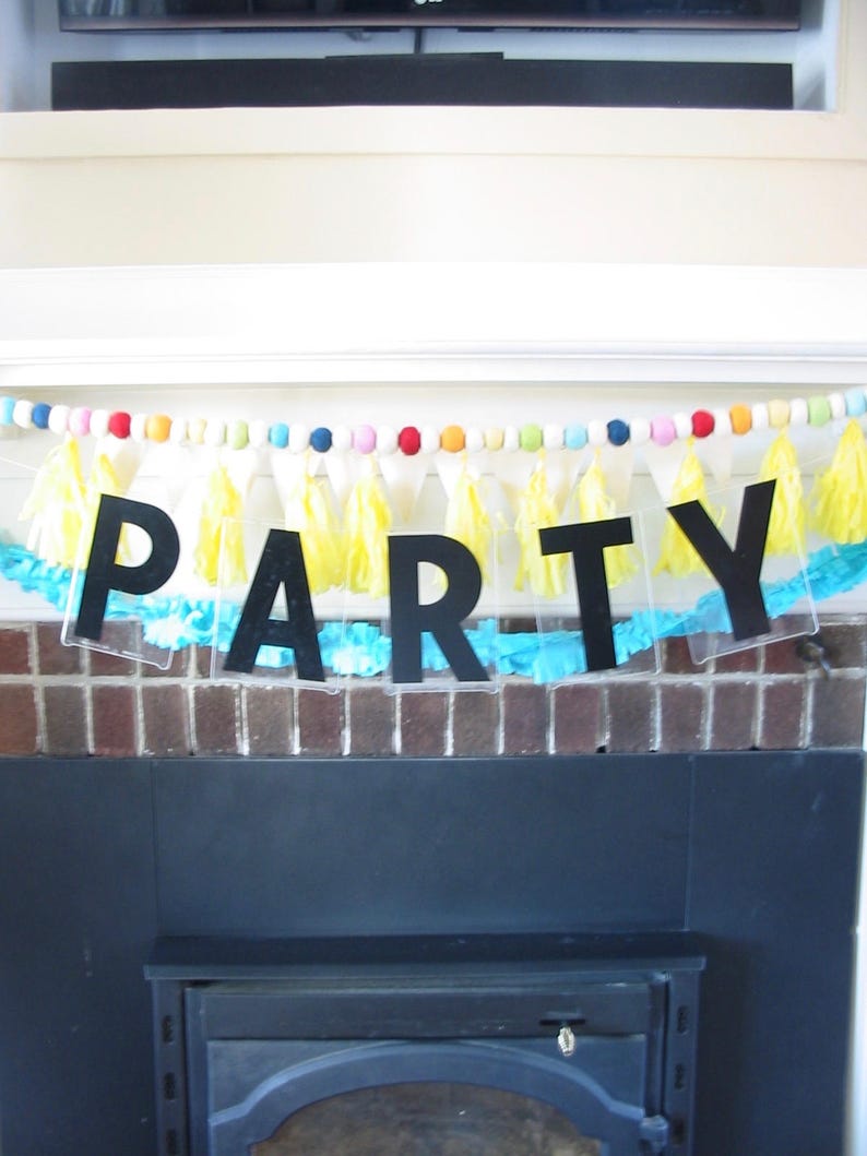 May include: A black and white party banner with the word "PARTY" in large, bold letters. The banner is decorated with yellow and blue tissue paper tassels and colorful beads.