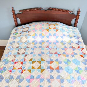 Puede incluir: Un edred&oacute;n hecho a mano con un dise&ntilde;o de patchwork colorido. El edred&oacute;n presenta una variedad de formas geom&eacute;tricas en colores pastel, incluyendo azul, rosa, naranja y amarillo. El edred&oacute;n est&aacute; extendido sobre un marco de cama de madera.