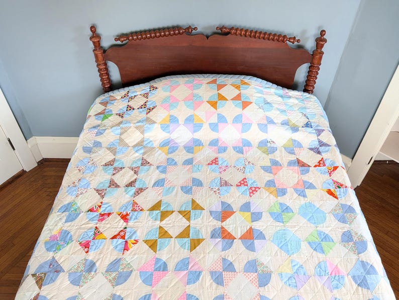 Puede incluir: Un edred&oacute;n hecho a mano con un dise&ntilde;o de patchwork colorido. El edred&oacute;n presenta una variedad de formas geom&eacute;tricas en colores pastel, incluyendo azul, rosa, naranja y amarillo. El edred&oacute;n est&aacute; extendido sobre un marco de cama de madera.