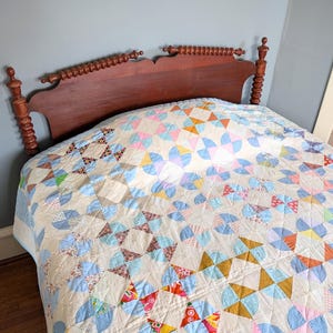 Puede incluir: Una colcha vintage con un colorido patr&oacute;n geom&eacute;trico cubre una cama. La colcha presenta una mezcla de formas azules, rosas, amarillas y naranjas sobre un fondo crema. El cabecero es de madera oscura.
