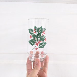 May include: A clear glass drinking glass with a green holly leaf and red berry design.
