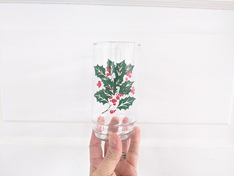May include: A clear glass drinking glass with a green holly leaf and red berry design.