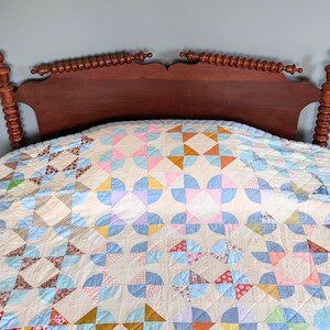 Puede incluir: Un edred&oacute;n hecho a mano con un dise&ntilde;o de patchwork colorido, con arcos y cuadrados en tonos pastel azul, rosa y amarillo. El edred&oacute;n est&aacute; sobre un cabecero de madera oscura, creando una escena de dormitorio acogedora.