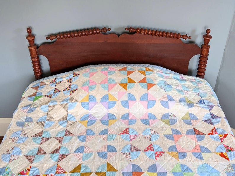 Puede incluir: Un edred&oacute;n hecho a mano con un dise&ntilde;o de patchwork colorido, con arcos y cuadrados en tonos pastel azul, rosa y amarillo. El edred&oacute;n est&aacute; sobre un cabecero de madera oscura, creando una escena de dormitorio acogedora.