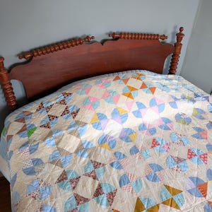 Puede incluir: Un marco de cama de madera con un acabado oscuro y un edred&oacute;n estampado. El edred&oacute;n presenta un dise&ntilde;o repetitivo de formas geom&eacute;tricas coloridas en tonos de azul, rosa, naranja y amarillo. La cama est&aacute; contra una pared azul claro.