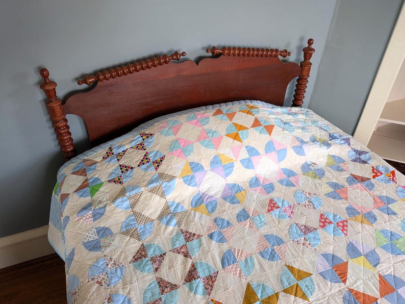 Puede incluir: Un marco de cama de madera con un acabado oscuro y un edred&oacute;n estampado. El edred&oacute;n presenta un dise&ntilde;o repetitivo de formas geom&eacute;tricas coloridas en tonos de azul, rosa, naranja y amarillo. La cama est&aacute; contra una pared azul claro.