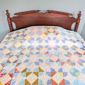 Puede incluir: Un edred&oacute;n hecho a mano con un dise&ntilde;o de patchwork colorido. El edred&oacute;n presenta un patr&oacute;n repetitivo de semic&iacute;rculos y tri&aacute;ngulos en tonos de azul, rosa, naranja y amarillo. El edred&oacute;n est&aacute; colocado sobre una cama con un cabecero de madera oscura.