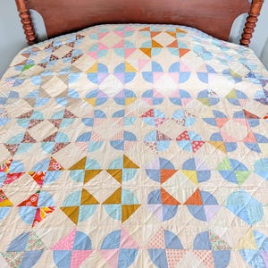 Puede incluir: Un edred&oacute;n hecho a mano con un patr&oacute;n repetitivo de formas coloridas en tonos de azul, rosa, naranja y amarillo. El edred&oacute;n est&aacute; colocado sobre una cama con un cabecero de madera. El dise&ntilde;o incluye semic&iacute;rculos y tri&aacute;ngulos.